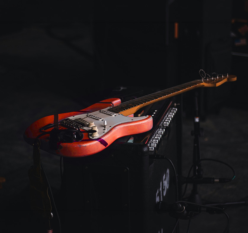 Close-up details of an electric guitar resting on an amp inside a dark professional rehearsal space.
